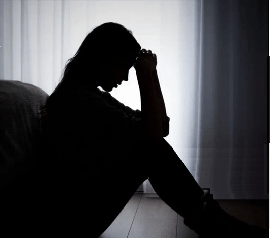 Personal Health Care Burnout warning photo of a woman sitting with both hands on her head in the dark to represent the signs of burnout