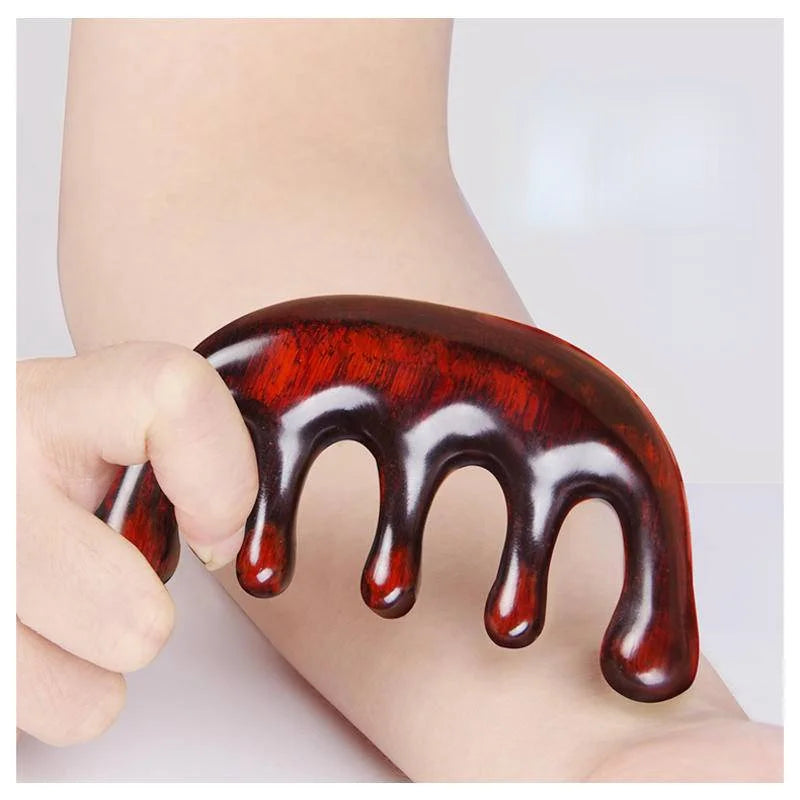 Massage Therapy Natural Wooden Massager Comb Picture show the comb in a woman hand above his arm. The comb, which has 5 large teeth, is a beautiful reddish-brown colour.
