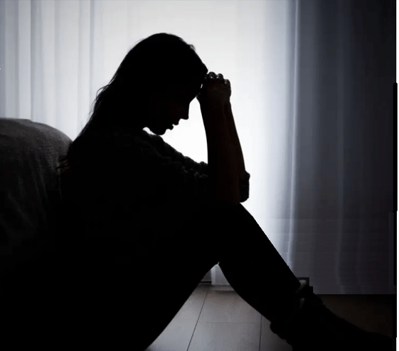 Personal Health Care Burnout warning photo of a woman sitting with both hands on her head in the dark to represent the signs of burnout