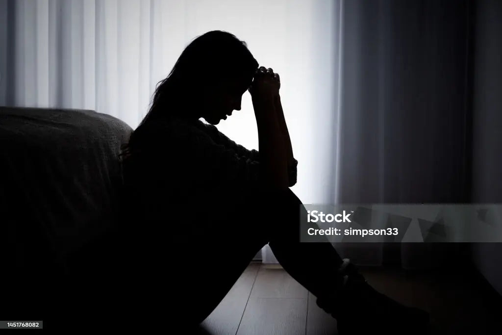 Personal Health Care Picture of a woman in semi-darkness sitting at the foot of a bed with both hands in a fist on her forehead and her elbows on her knees. Blog Preventing Personal Burnout   
