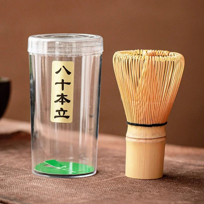 Massage Therapy Accessories Japanese Geisha Tea Set Matcha Whisk Picture of the whip and its plastic container with Japanese inscriptions placed on a woven bamboo doily on a wood table