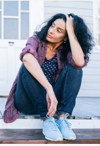 Personal Health Care, Picture of a woman in her fifties wearing blue canvas shoes, sitting on the steps of a cottage with one hand in her hair and her arm flapping in her lap, looking tired, Blog: How to live more easily with menopause symptoms?